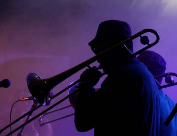 A musician playing a trombone with smoke and purple lighting in the background
